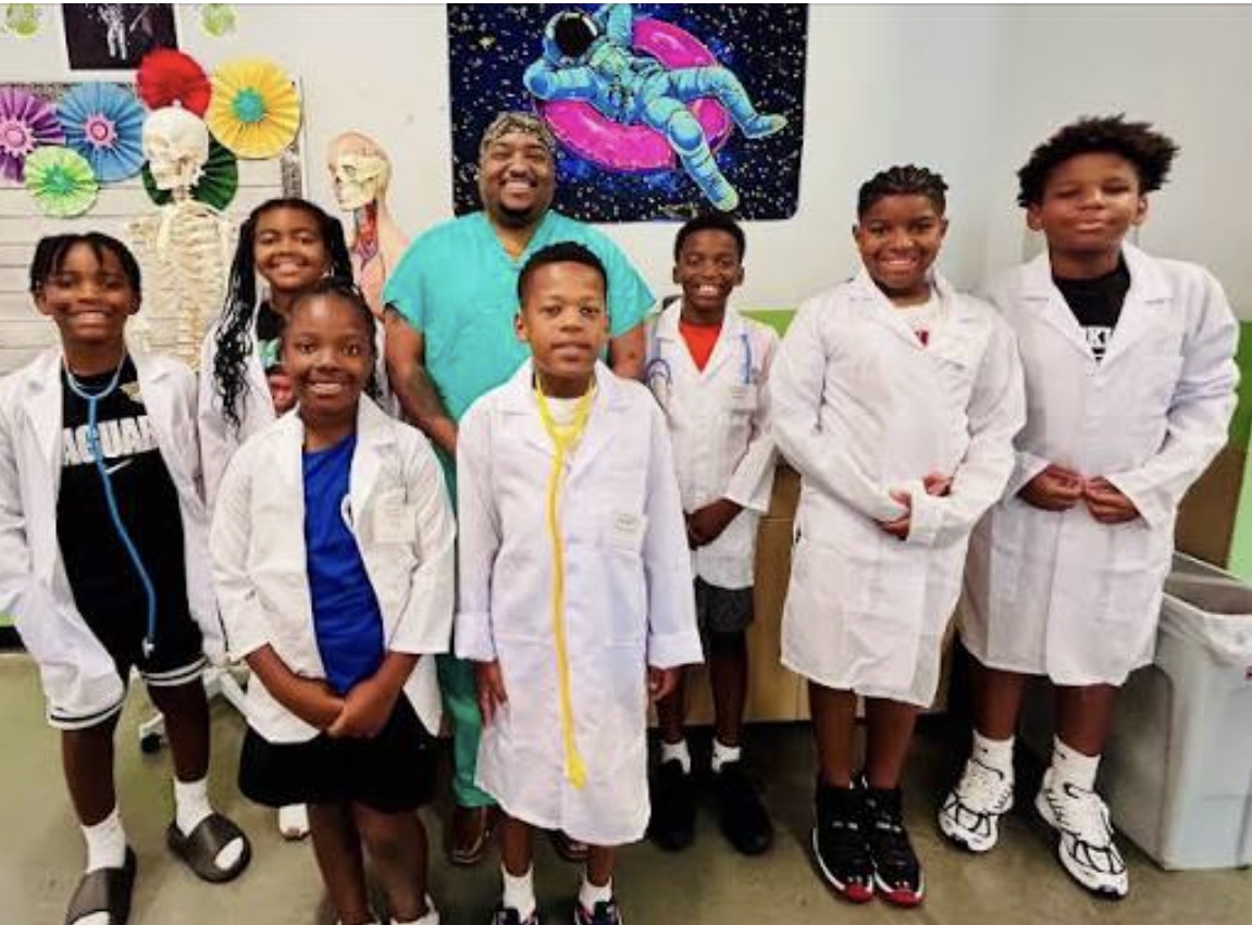 Founder with young students wearing white lab coats in a classroom